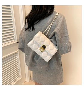 Detail of white quilted crossbody bag with golden oval twist lock and chain strap