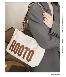 Close-up of beige canvas tote with brown leather lettering and metal chain strap