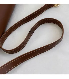Detail showing smooth brown leather shoulder strap with cream stitching and gold buckle