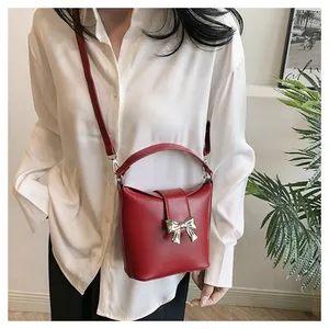 Close-up of a red bucket bag featuring a decorative gold bow clasp and smooth leather