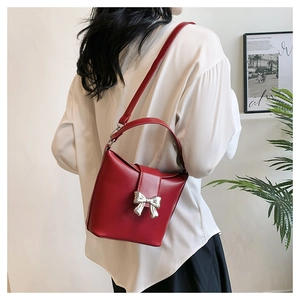 Detailed view of a red leather bucket bag with a silver bow clasp worn by a model