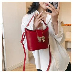 Red bucket bag with a golden bow clasp and crossbody strap shown on a white shirt
