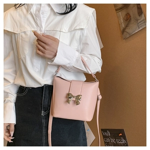 Pink bucket bag with gold bow clasp shown by a model for a chic French style look