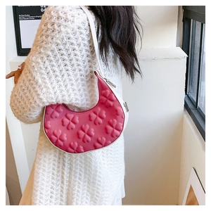 Pink crescent underarm bag with embossed clover patterns and white shoulder strap