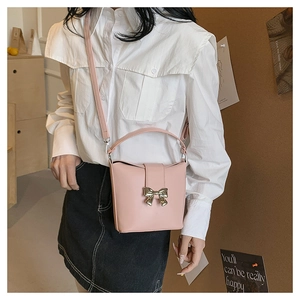 Detail of light pink mini bucket bag with gold bow clasp and thin leather shoulder strap