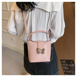 Pink bucket bag with silver bow accent and adjustable shoulder strap worn by a model