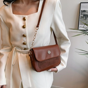 Brown PU leather crossbody bag with metal emblem shown on model in vintage cream dress