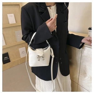 Detail of white bucket bag with silver bow clasp on a lifestyle wooden shelf setting