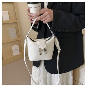 Close-up of a white bucket bag with silver metal bow detail and detachable shoulder strap