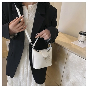 White bucket bag with silver bow accent shown on model with chic black and white outfit