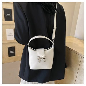 Detail of white bucket bag with silver bow accent shown on model in minimal setting