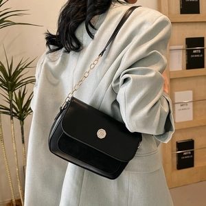Detail of a black leather crossbody bag featuring silver logo and gold chain strap