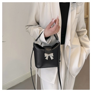 Detail of a chic black bucket bag with a silver metal bow and adjustable crossbody strap