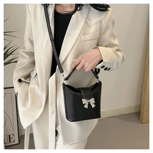 Detail of a black leather bucket bag featuring a silver bow accent and slim shoulder strap