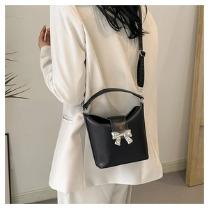 Black leather bucket bag with silver bow accent shown on model in white blazer