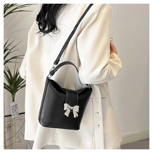 Detail of a black bucket bag with a silver metal bow accent and matte leather finish