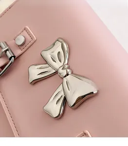 Close-up of pink leather crossbody bag with silver bow ornament and stitching detail