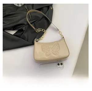 Detail of beige patent leather hobo bag featuring butterfly embossing and metal chain strap