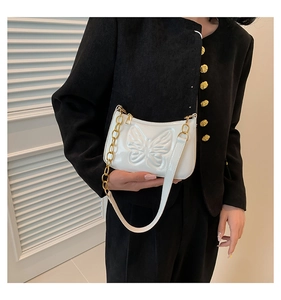 Close-up of white patent leather underarm bag featuring embossed butterfly and gold chain