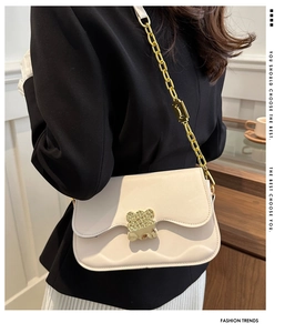 Close-up of cream saddle bag featuring golden geometric lock and chunky chain strap