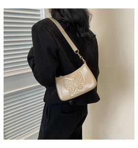 Detail of a beige patent leather shoulder bag with embossed butterfly and slim strap