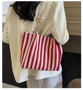 Detail of red and white striped tote bag with gold chain strap worn by a model