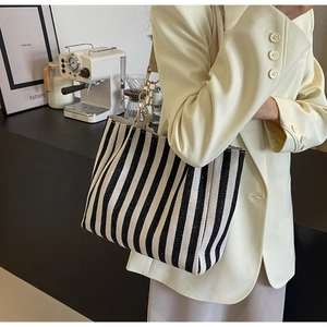 Detail of striped canvas tote bag with chain strap shown on a woman in a beige blazer