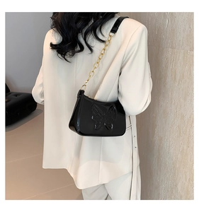 Detail of black glossy patent leather shoulder bag with embossed butterfly and gold chain