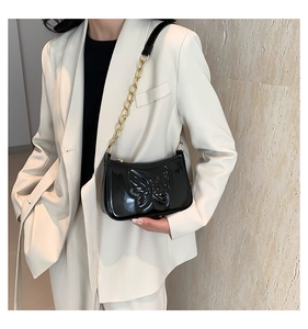 Detail of black patent leather underarm bag with 3D butterfly and gold chain strap
