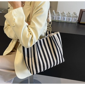 Detail of striped canvas tote bag with gold chain strap on beige suit shoulder