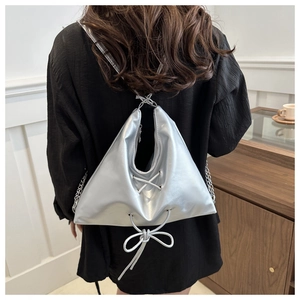 Detail showing metallic silver triangular backpack with lace-up bow and chain strap