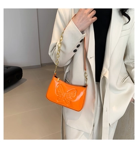 Detail of orange patent leather shoulder bag with embossed butterfly and gold chain strap