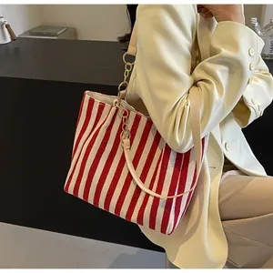 Detail of red and white striped canvas tote bag with leather strap and gold chain link