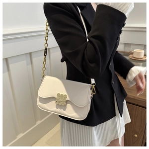 Detail of white saddle bag featuring a gold bear clasp and hybrid chain strap
