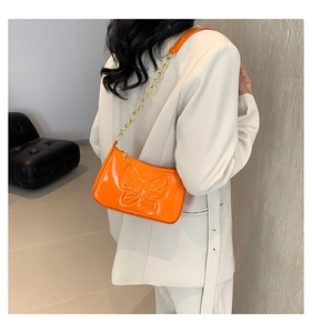 Detail of glossy orange patent leather bag with embossed butterfly and gold chain strap