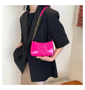 Detail of rose pink patent leather shoulder bag featuring butterfly relief and gold chain