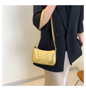 Detail of gold patent leather shoulder bag featuring embossed butterfly design and chain strap