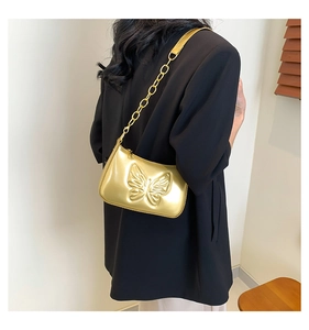 Detail of a metallic gold shoulder bag with a large embossed butterfly and chain strap