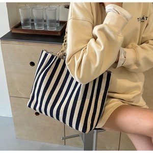 Detailed view of striped tote bag with woven texture and gold chain strap shown on model