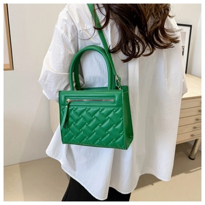 Detail of green quilted square handbag with metal zipper worn by a woman over a white shirt