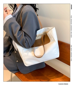 Close-up of a large white PU tote bag with brown leather handles and FASHION embossed logo