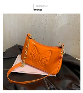 Detail of vibrant orange patent leather underarm bag with embossed butterfly and gold chain