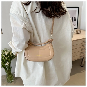 Detail of a beige half-moon crossbody bag featuring a unique knotted handle and gold text