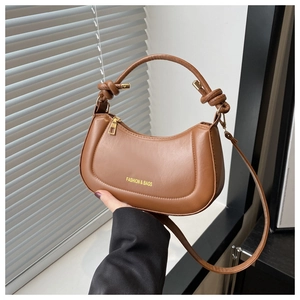 Detail of a brown crescent saddle bag featuring a unique knotted handle and gold text