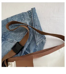 Dettaglio della borsa tote in tela con bordo marrone e tracolla regolabile su denim