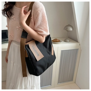 Dettaglio borsa tote in tela nera con tracolla marrone e logo fashion sulla tasca