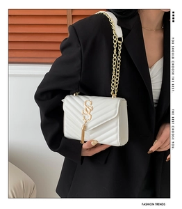 Detail of white quilted crossbody bag with golden SSS logo and metal tassel accent