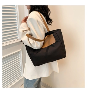 Detail of a large black nylon tote bag with brown leather handles worn by a model