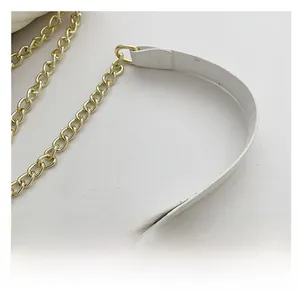 Detail shot of light gold metal chain strap with white leather shoulder piece for cross-body bag