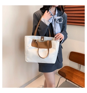 Detailed shot of large capacity color-block tote bag with brown leather handles and text